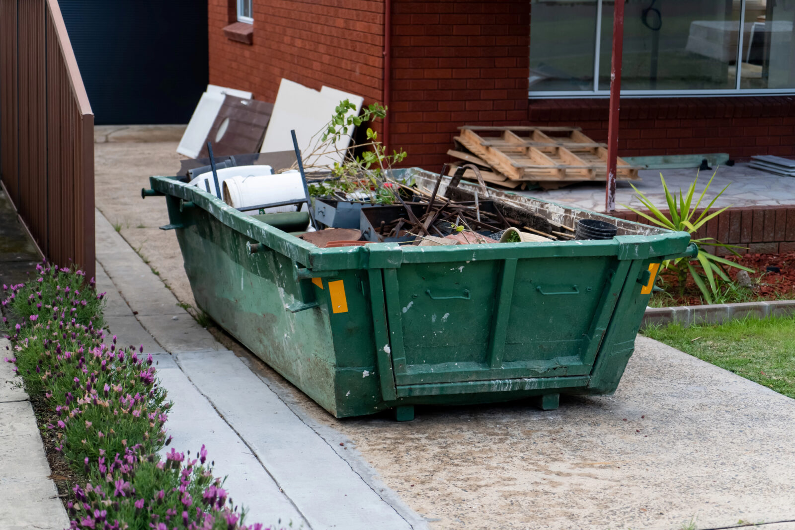 Groene grofvuilcontainer gevuld met oude spullen op een oprit