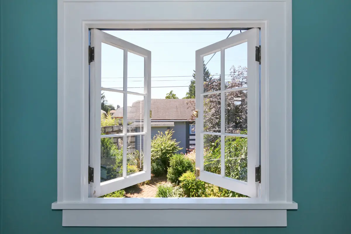 Openstaand wit raamkozijn met uitzicht op een groene tuin