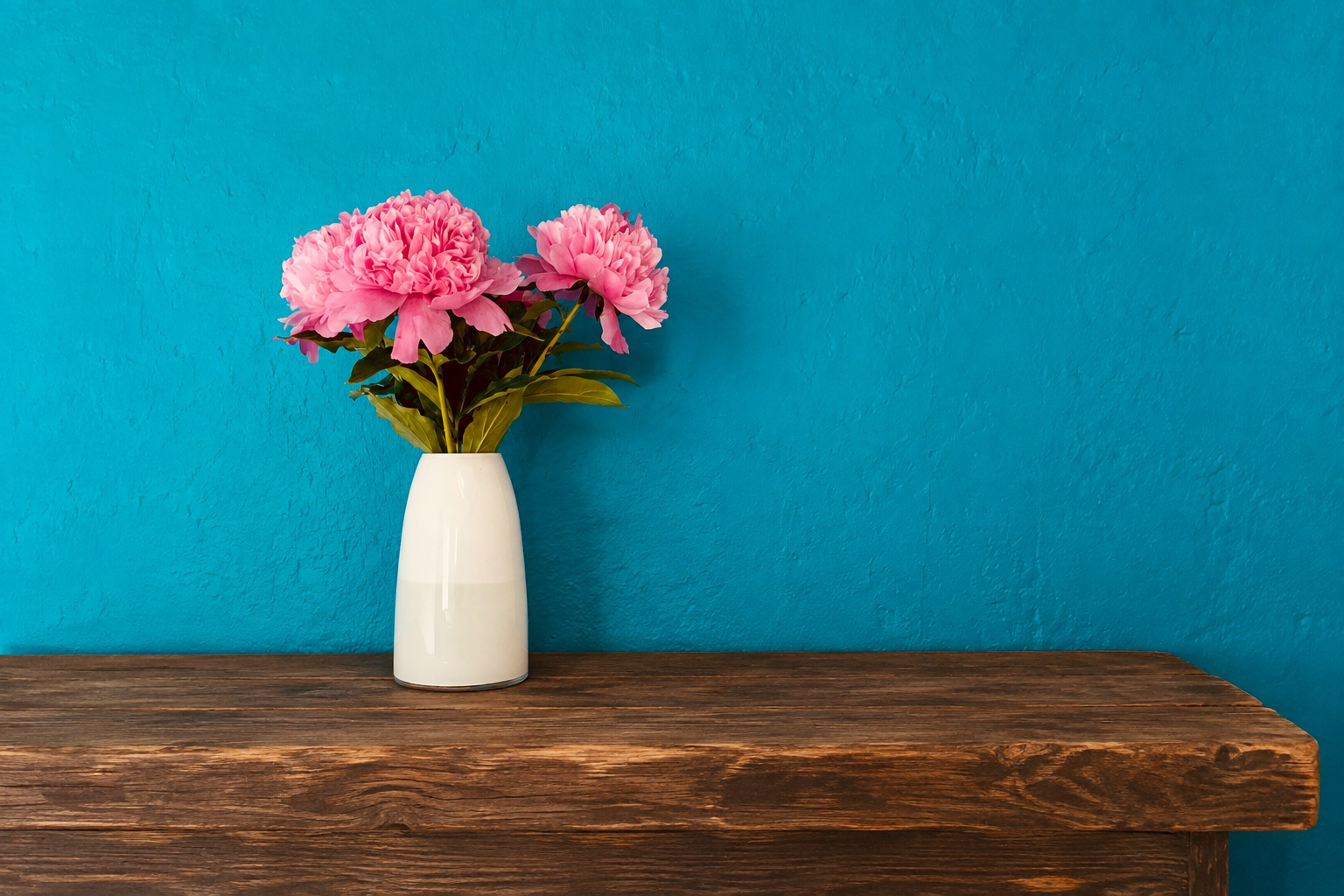Roze pioenrozen in een witte vaas tegen een blauwe muur