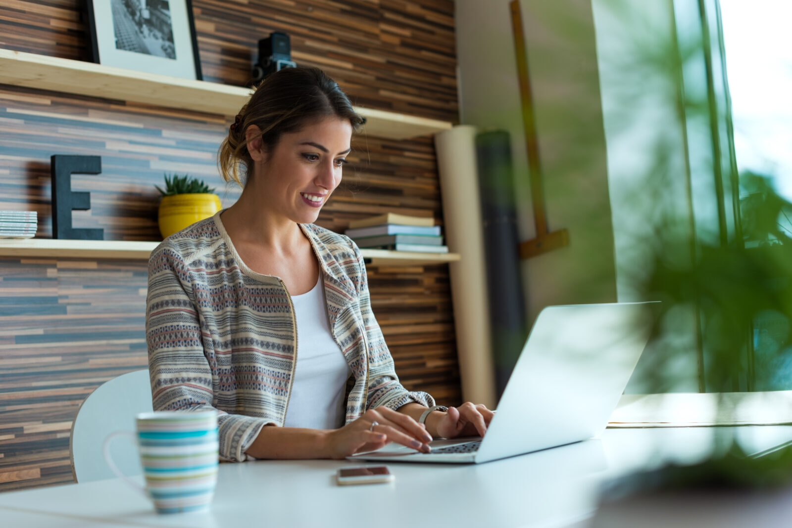 Vrouw werkt op een laptop aan een witte tafel bij het raam.