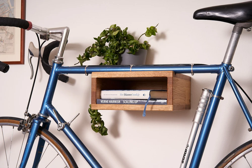 Blauwe racefiets aan houten fietshanger met boeken en plant