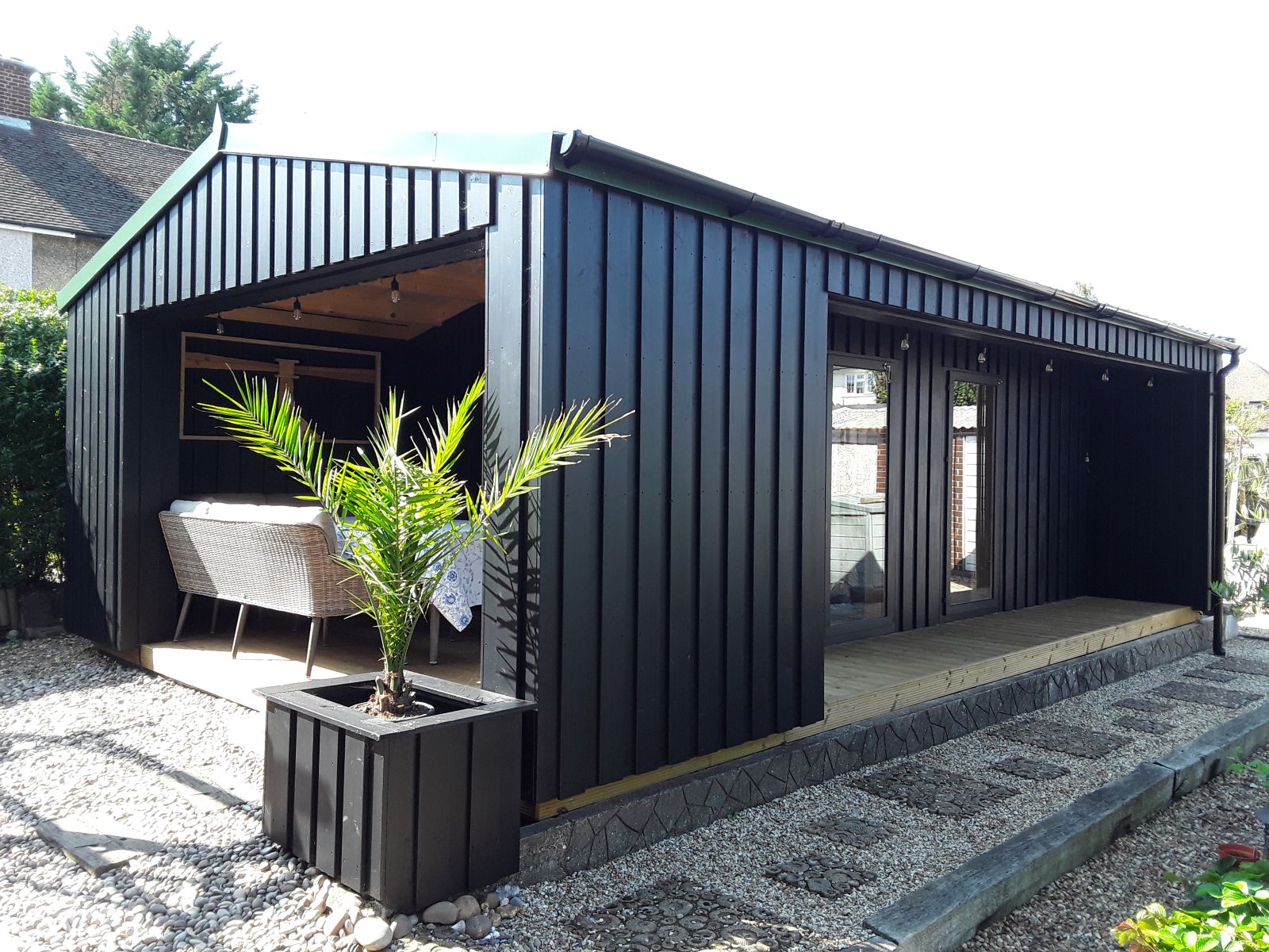 Zwart houten tuinhuis met overkapping, overdekte zitplek en glazen deuren in de tuin