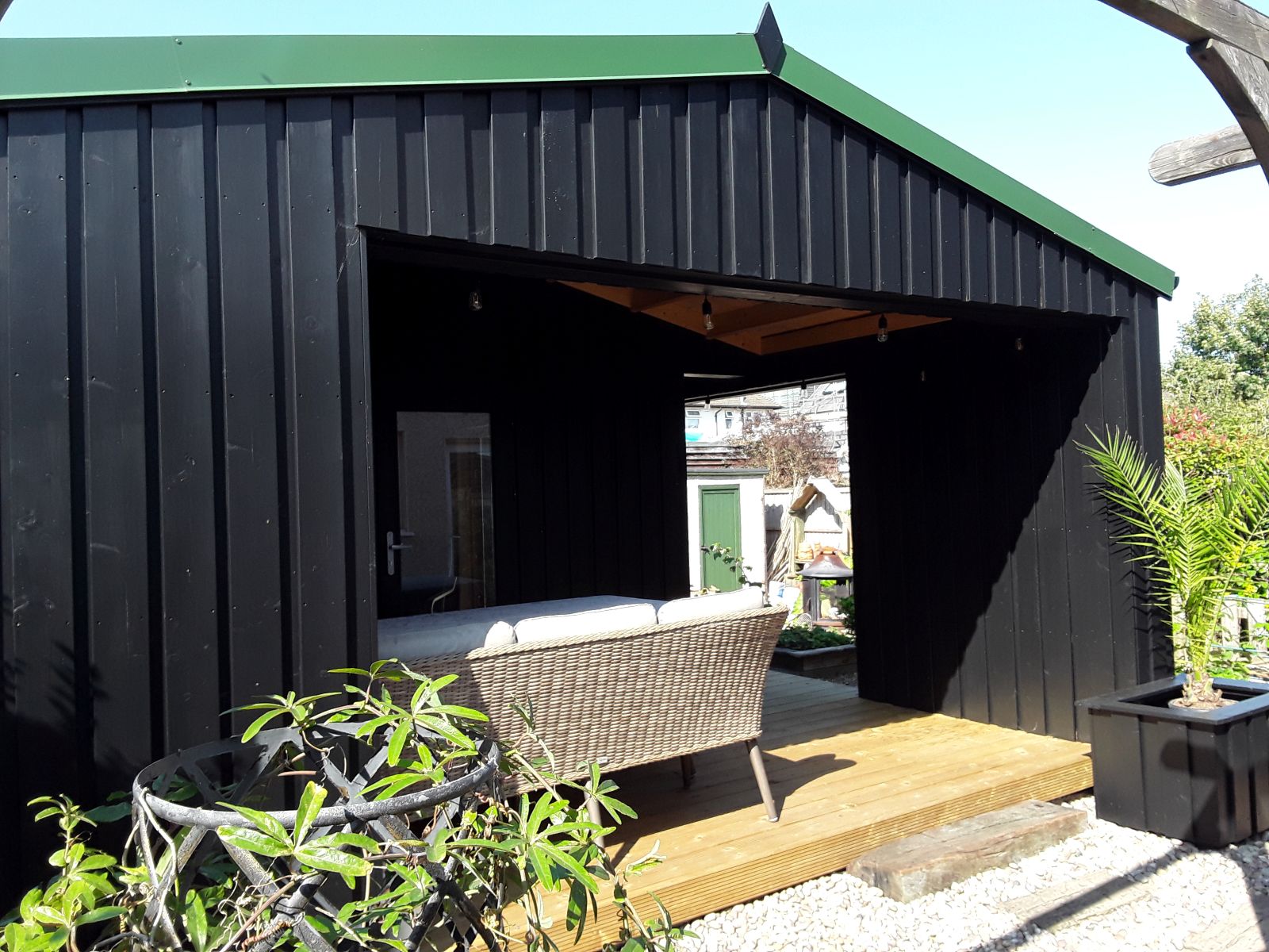 Overdekte zitplek met tuinbank en houten vlonder bij een zwart houten tuinhuis